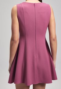 Une robe sans manches évasée en tissu texturé rose profond, avec une fermeture éclair étroite dans le dos et des coutures ajustées pour la structure.