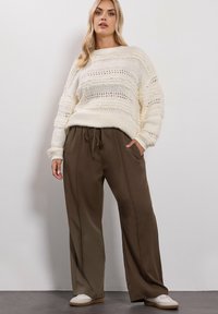 Stickad krämfärgad tröja med strukturerade ränder och vida bruna byxor. Byxorna har dragsko i midjan och sidofickor, i kombination med vita sneakers.