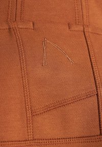 Tkanina v rustikálnej farbe má jemnú štruktúru s kontrastným prešívaním. Viditeľné je aj výnimočné výšivkové logo, ktoré zvýrazňuje detaily dizajnu.
