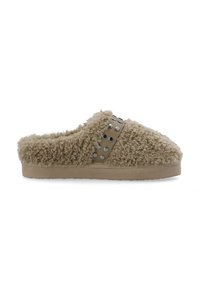 Fuzzy beige hjemmesko med en blød, tekstureret overdel, en rund tå og en dekorativ rem med cirkulære metalaccentuer. Flad sål.