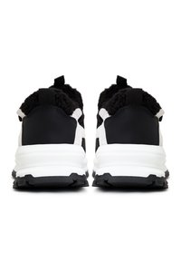 Baskets noir et blanc avec semelles blanches épaisses, tige noire texturée et languettes au talon, vues de dos.