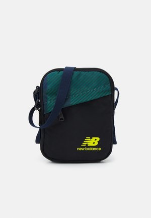 Kompakte schwarze und grüne Umhängetasche mit verstellbarem marineblauem Riemen, vordere Reißverschlusstasche und neon-gelbem New Balance Logo.