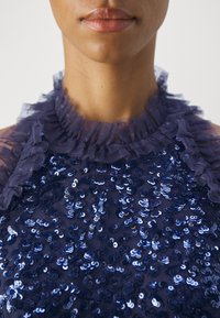 Gros plan sur le cou et les lèvres portant un haut bleu marine à sequins avec un col haut en tulle froncé.
