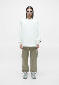 Hvid oversized sweatshirt, lysebrune cargo bukser, sølvfarvede sneakers og hvide solbriller. Simpelt design med en afslappet pasform og praktiske lommer.