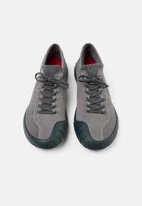 Le scarpe sportive in maglia grigia presentano una parte superiore in rete testurizzata, punta arrotondata e una suola in gomma scura con un motivo di presa unico. Accenti interni rossi.