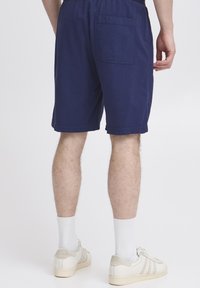 Marineblå bomullsshorts med elastisk midje, sidelommer og én baklomme. Avslappet lengde over kneet.