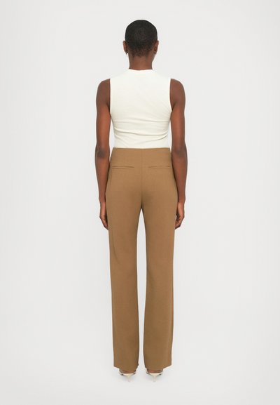 Fitted white sleeveless top paired with high-waisted, straight-leg brown trousers. Trousers feature two back pockets and clean lines.
