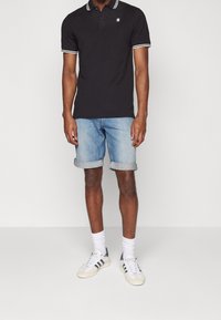 Černé polo tričko s límečkem se bílými proužky, doplněné o světlé modré džínové kraťasy s ohrnutými lemy a bílé tenisky se šedými detaily.