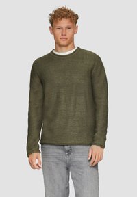 Olive green sweter dzianinowy z okrągłym dekoltem, teksturowana tkanina i długie rękawy, połączony z jasnoszarymi dżinsami.