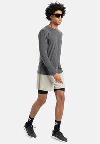 Grå långärmad tröja, ljusbeiga shorts med logotyp, svarta kompressionsshorts under, och svarta sneakers med vita sulor. Svarta solglasögon.