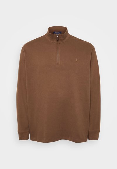 Ruda ilgomis rankovėmis polo marškiniai su aukštu apykakle, su ketvirčio užtrauktuku. Minkšta tekstūra, mažas logotipo akcentas ant krūtinės.