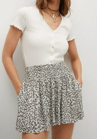 Top blanco de manga corta con textura acanalada y botones, combinado con una falda negra con estampado floral, bolsillos y cintura fruncida.