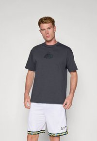 Siva kratka majica s kratkimi rokavi zatemnjenim logotipom na prsih, kombinirana z belimi kratkimi hlačami z barvnim vzorčastim robom.