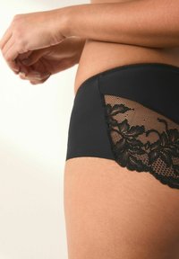 Schwarze Unterwäsche mit einer glatten Stofffront und aufwendigen schwarzen Spitzenverzierungen an der Seite. Die Spitze weist florale Muster und ein Mesh-Design auf.