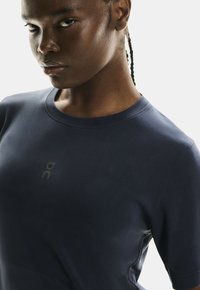 Sötétkék sportpóló rövid ujjakkal, kerek nyakkivágással és egy diszkrét logónyomattal az elején. Simma, textúrált anyag.