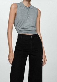 Polo sin mangas gris con cuello y tres botones, combinado con unos pantalones vaqueros negros de pierna ancha y talle alto, que enfatizan las líneas limpias y el diseño simple.