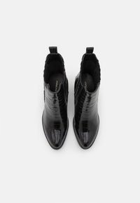 Bottes noires pour la cheville en matériau embossé effet crocodile brillant. Dotées d'un bout pointu et de panneaux latéraux élastiques pour un enfilage facile.