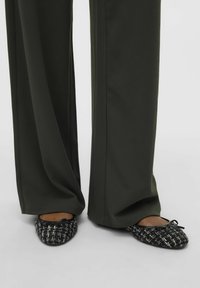 Sorte og hvite tweed ballerinas med sløyfedetalj, kombinert med løse, mørkegrønne vide bukser. Flatt såle, teksturert stoff.