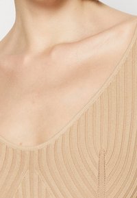 Haut en maille beige clair avec un col rond, présentant une texture à côtes verticales et un discret détail de couture horizontale.