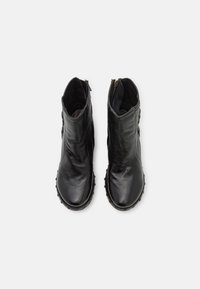 Botas de tobillo de cuero negro con un acabado suave, punta redondeada, cremallera lateral y suela texturizada con pequeñas tachuelas para un mejor agarre.