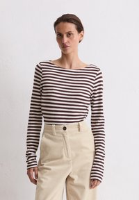 Długi rękaw, sweter w poziome brązowe i białe paski, zestawiony z beżowymi spodniami z korduroju o wysokim stanie z zapięciem na guzik.