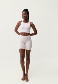 Ljusrosa träningsoverall består av en åtsittande sport-bh och högmidjade shorts, med en slät textur och minimalistisk design.