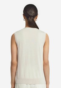 Ljust beige ärmlös stickad topp med rund hals och ribbad nederkant, med en mjuk yta och minimalistisk design.