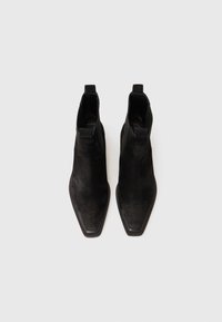 Bottes noires en daim au niveau de la cheville avec un design à bout pointu, un talon plat et des languettes à l'arrière, mettant en avant une texture lisse et un style minimaliste.