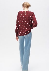 Bordeaux blouse met witte stippen, sleutelgat achter, lange mouwen, gecombineerd met lichtblauwe wijde jeans. Gladde stof, ontspannen fit.