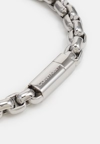 Ezüst rozsdamentes acél lánc karkötő fényes, összekapcsolt szemekkel és a "Calvin Klein" márkanevével gravírozott csattal.