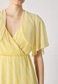 Yellow chiffon dress with a v-neck and flutter sleeves, featuring a pleated texture and an elastic waistband for a flowing silhouette.