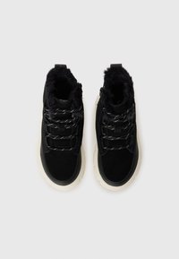 Bottes noires en daim à la cheville avec bordure en fausse fourrure, comportant des lacets noir et blanc, une semelle épaisse de couleur crème et un design à bout rond.