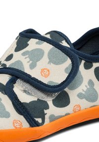 Stoffschuh mit hellbeigem Hintergrund, dunkelgrünem Muster und orangefarbenen Akzenten. Mit einem Klettverschluss und einer strukturierten orangenen Sohle.