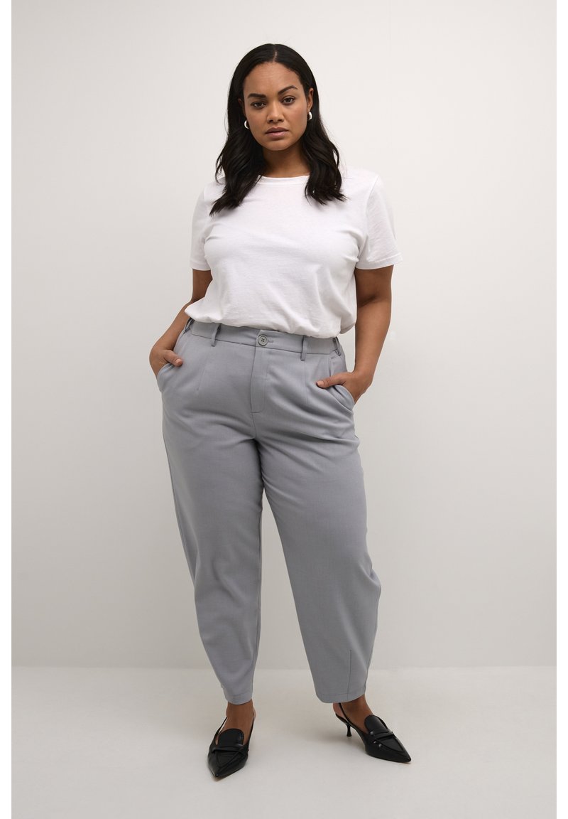 Pantaloni grigi su misura con una vestibilità rilassata e tasche laterali, abbinati a una maglietta bianca. Scarpe nere a punta completano l'outfit.