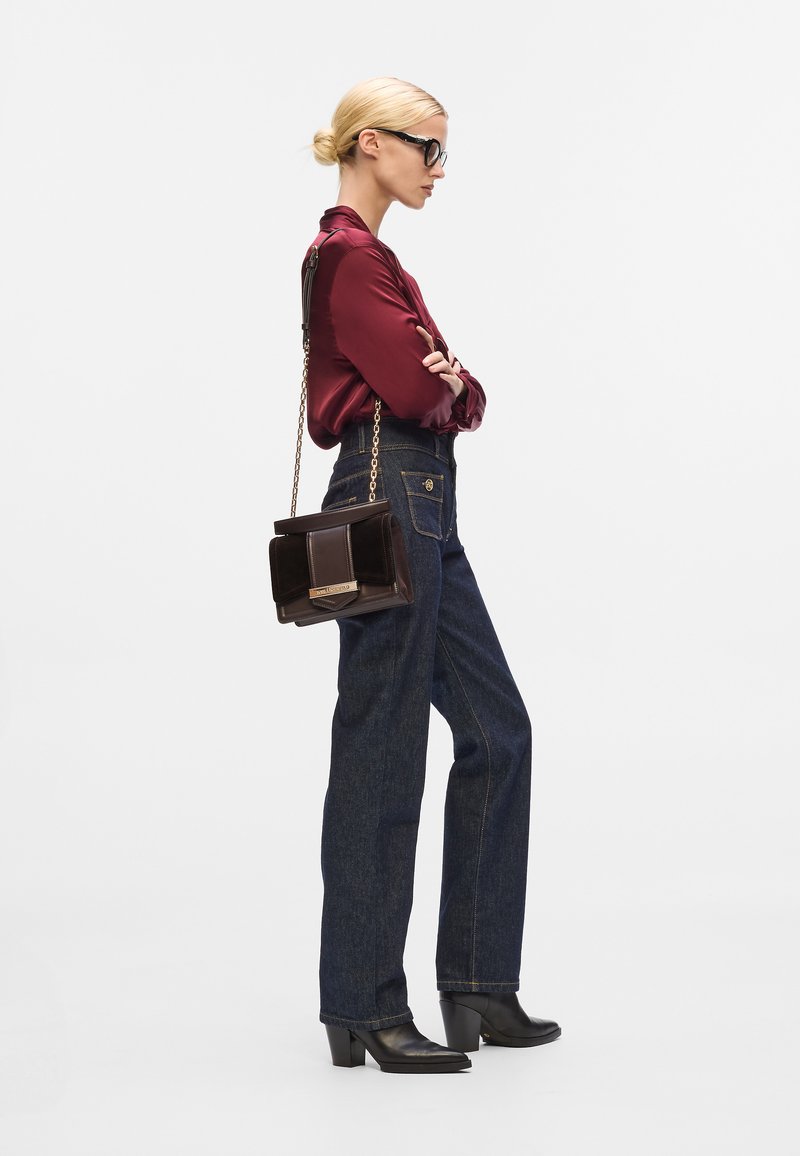Bordeaux satijnen blouse, hoge taille donkere spijkerbroek, zwarte haklaarzen en een bruine schoudertas met een kettinghengsel.