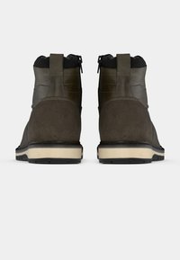 Botas de ante marrón oscuro con parte superior de cuero liso, que cuentan con un cierre de cremallera y una suela gruesa y texturizada para mayor tracción.