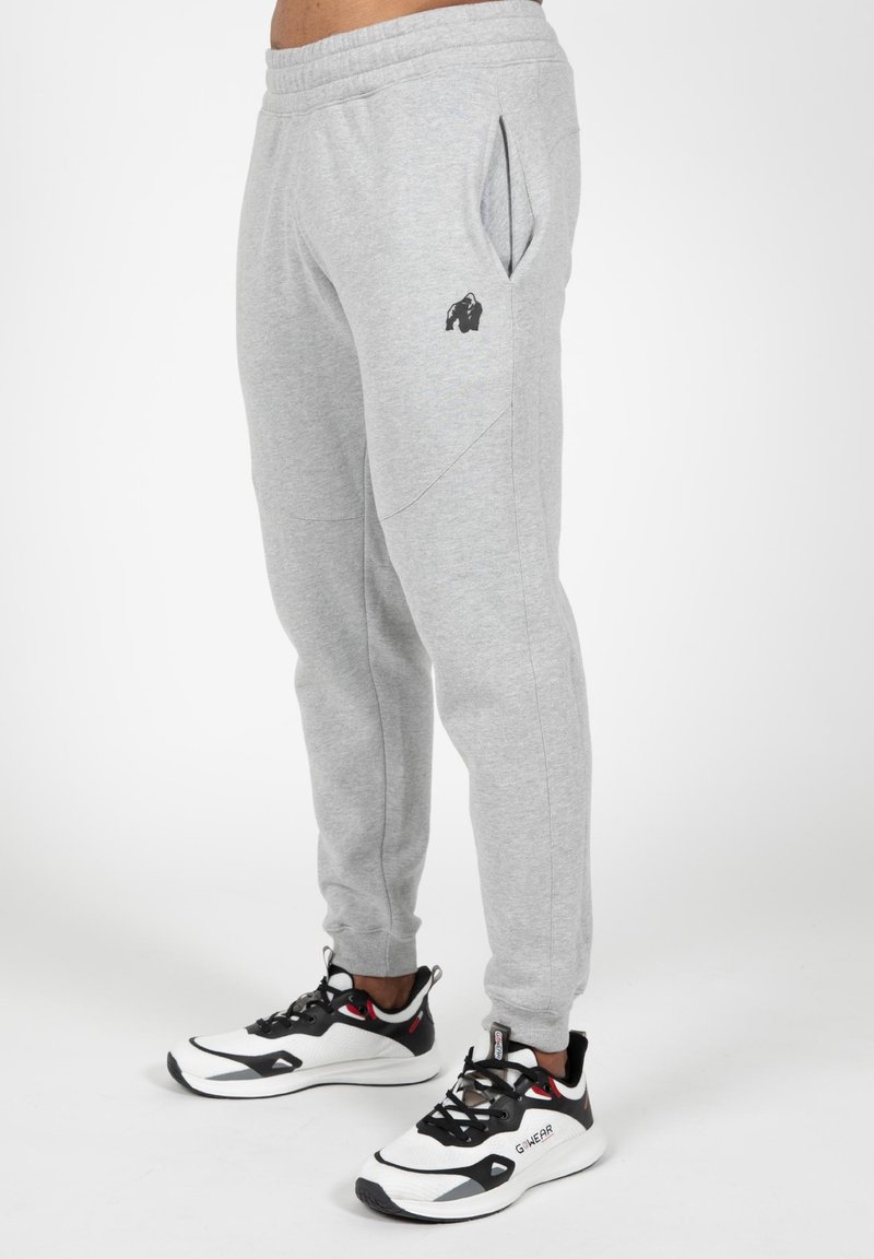 Grijze joggingbroek met zijzakken, taps toelopende fit, elastische tailleband en een zwart logo op het linkerenbeen. Gemaakt in combinatie met zwart-witte sport sneakers.