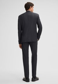 Donkergrijze suit met een op maat gemaakte pasvorm, voorzien van een lange jas, gestructureerde schouders en slanke broeken; zachte stof met minimale details.
