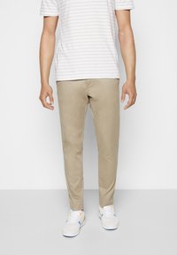 Chinos beige de algodón, diseño tapered, combinados con una camisa a rayas blanca y gris claro, y zapatillas blancas con acentos de color.