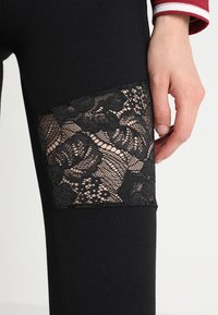 Leggings noirs avec un panneau en dentelle transparente à la cuisse avec des motifs floraux et une taille noire unie. Tissu doux et extensible.