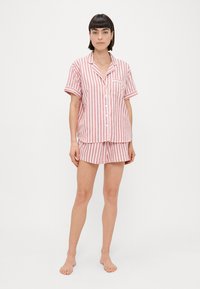 Ensemble de pyjama léger rayé en rose et blanc. Haut à boutons à manches courtes avec poche, short assorti avec taille élastique. Texture de tissu lisse.