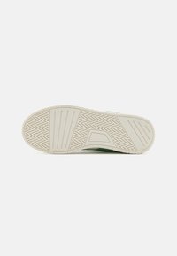 Semelle de sneaker blanche avec une surface en caoutchouc texturé et un motif en chevrons, dotée d'accents verts sur le dessus et d'une forme épurée.