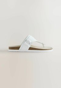 Sandale blanche à lanière large en cuir, boucle métallique circulaire, semelle intérieure en liège et semelle extérieure en caoutchouc blanc sur fond neutre.