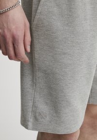 Grå teksturerede shorts med et diskret ribbet mønster, der har sidelommer og et logo-detalje nær sømhåndtaget. Blødt materiale, afslappet pasform.