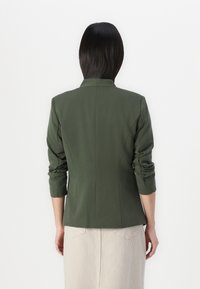 Groene op maat gemaakte blazer met een gestructureerde pasvorm, driekwart mouwen en een notch-kraag. Glad materiaal met schone naden en een minimalistisch ontwerp.