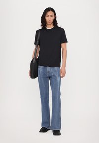 Svart kortermet t-skjorte, blå vide jeans og svarte lær sko. Modellen bærer en svart skulderveske med en glatt tekstur.