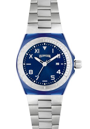Montre analogique bleue avec un bracelet en acier inoxydable, un boîtier rond et un cadran texturé bleu avec des accents argentés et des index horaires.