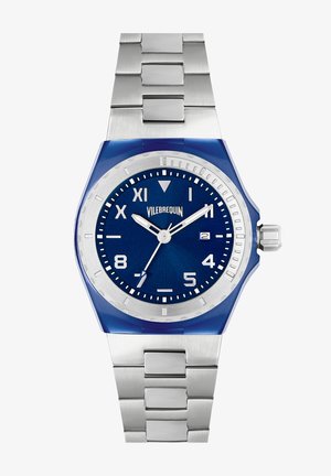 Montre analogique bleue avec un bracelet en acier inoxydable, un boîtier rond et un cadran texturé bleu avec des accents argentés et des index horaires.