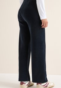 Pantaloni a gamba larga in corduroy navy con una texture a coste, dotati di tasca posteriore e vestibilità comoda. Abbinati a sneaker basse.