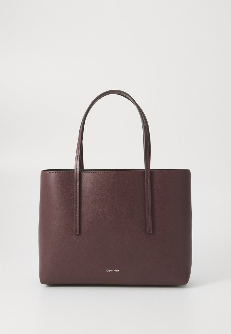 Sac fourre-tout en cuir bourgogne avec deux anses fines, design minimaliste et logo en relief sur le devant. Forme plate avec texture lisse.